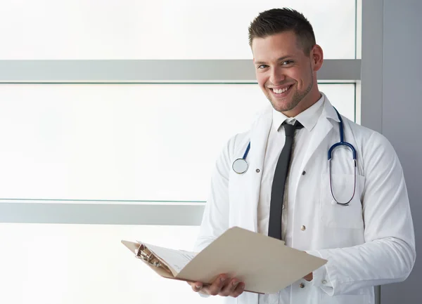 Portrait of a male doctor holding his patient chart in bright modern hospital — Stok Foto