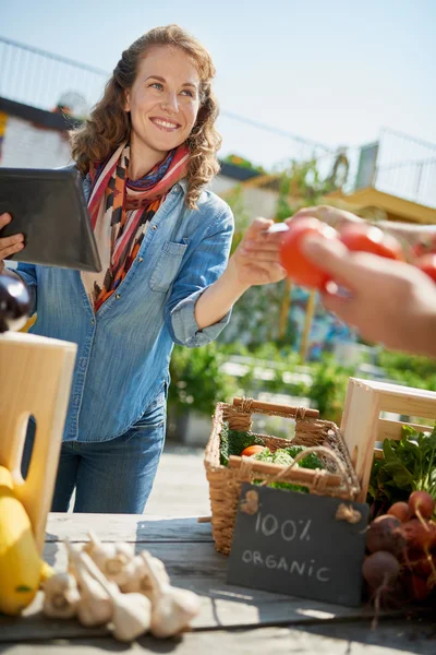 Donna amichevole che cura una bancarella di verdure biologiche in un mercato agricolo e vende verdure fresche dall'orto sul tetto — Foto Stock