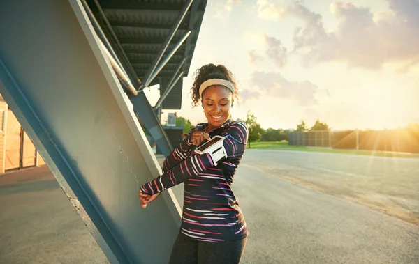 Mujer afroamericana en forma eligiendo la música de una aplicación para correr al atardecer —  Fotos de Stock