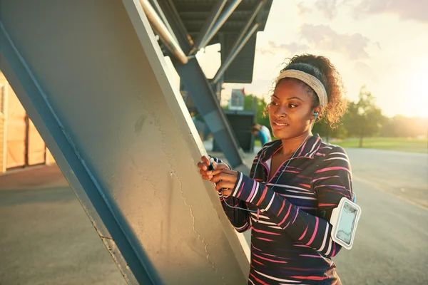 Mujer afroamericana en forma eligiendo la música de una aplicación para correr al atardecer —  Fotos de Stock