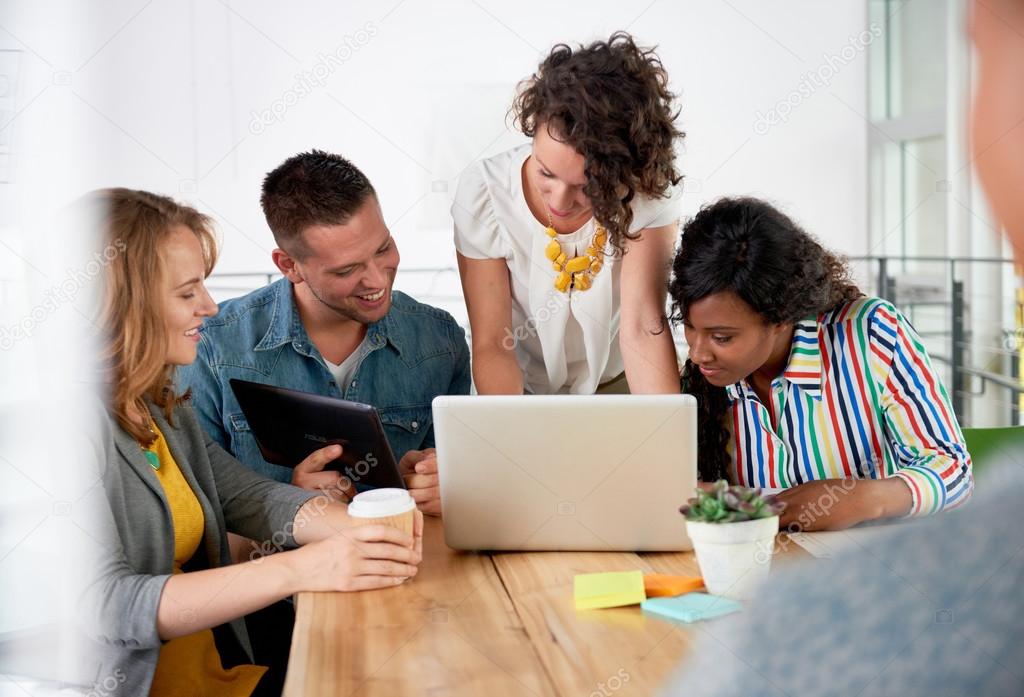 Multi ethnic group of succesful creative business people using a laptop during candid meeting