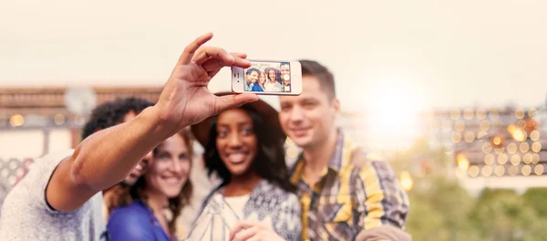 Grupo multi-étnico milenar de amigos tirando uma foto selfie com telefone celular no terraço do telhado ao pôr do sol — Fotografia de Stock