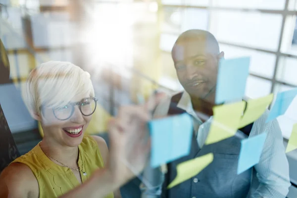 Dos propietarios de pequeñas empresas milenarias creativas que trabajan en una lluvia de ideas de estrategia de redes sociales utilizando notas adhesivas en ventanas —  Fotos de Stock