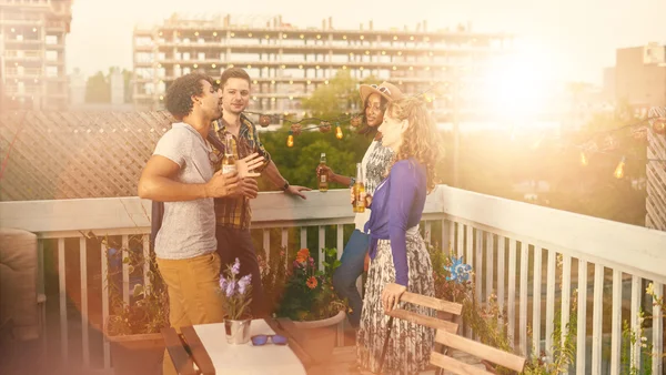 Multi-ethnic millenial group of friends partying and enjoying a beer on rooftop terrasse at sunset — Stock Photo, Image