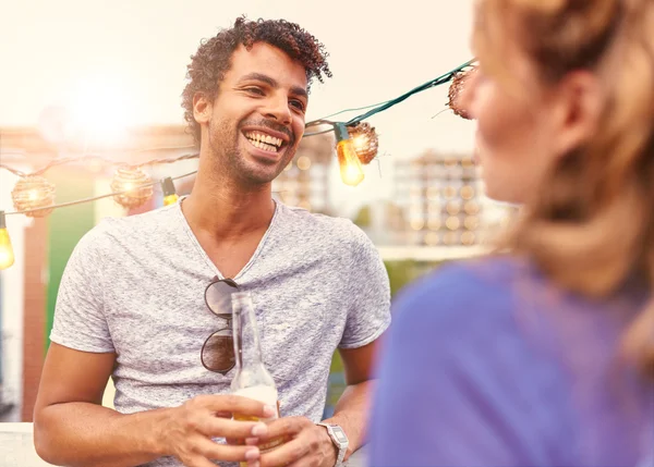 Multi-ethnic millenial couple flirting while having a drink on rooftop terrasse at sunset — Stock Photo, Image
