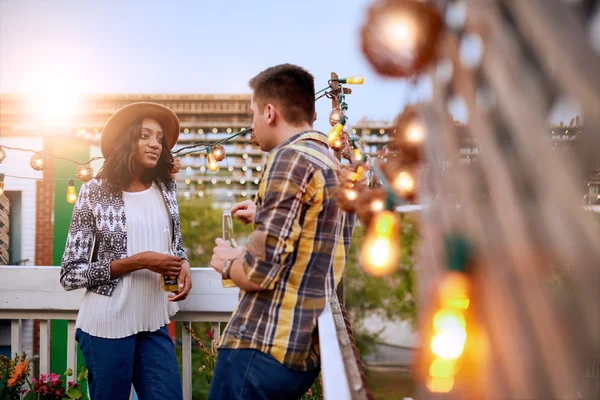 Multi-étnica pareja millenial coqueteando mientras toma una copa en la terraza de la azotea al atardecer — Foto de Stock