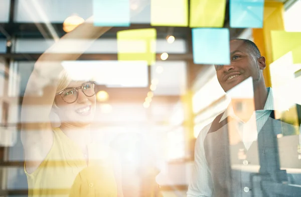 Dos propietarios de pequeñas empresas milenarias creativas que trabajan en una lluvia de ideas de estrategia de redes sociales utilizando notas adhesivas en ventanas — Foto de Stock