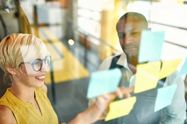 Two creative millenial small business owners working on social media strategy brainstorming using adhesive notes in windows — Stock Photo, Image