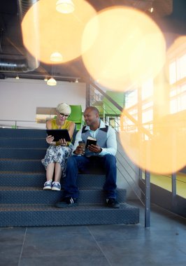 Merdiven otururken bir dijital tablet kullanarak sosyal medya stratejisi üzerinde çalışan iki yaratıcı millenial küçük işletme sahipleri