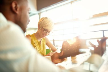 Masa başında otururken bir dijital tablet kullanarak sosyal medya stratejisi üzerinde çalışan iki yaratıcı millenial küçük işletme sahipleri