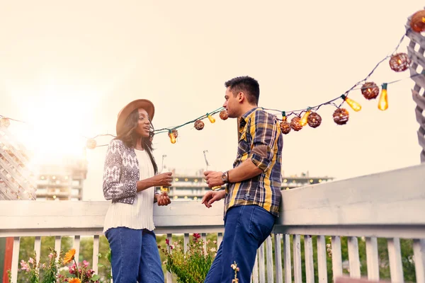 Multi-étnica pareja millenial coqueteando mientras toma una copa en la terraza de la azotea al atardecer — Foto de Stock