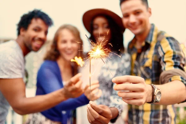 Grupo multi-étnico milenar de amigosdobrando sparklers no terraço no telhado ao pôr do sol — Fotografia de Stock