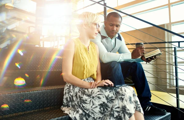 Two creative millenial small business owners working on social media strategy using a digital tablet while sitting in staircase — Stock Photo, Image