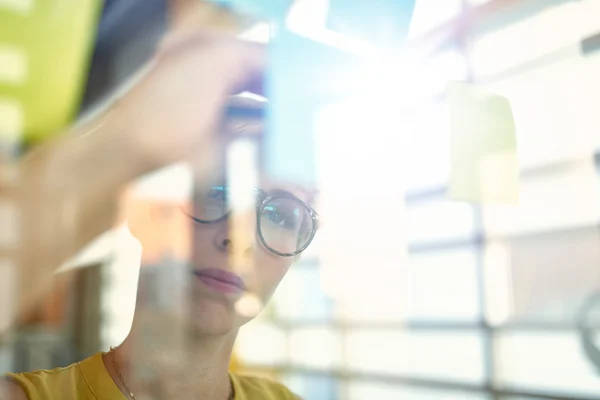 Two creative millenial small business owners working on social media strategy brainstorming using adhesive notes in windows — Stock Photo, Image