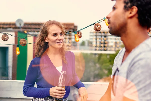 Casal milenar multi-étnico flertando enquanto toma uma bebida no terraço do telhado ao pôr-do-sol — Fotografia de Stock