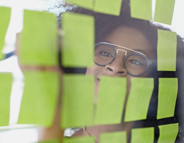 Portrait of a business woman with an afro behind sticky notes in bright glass office clipart