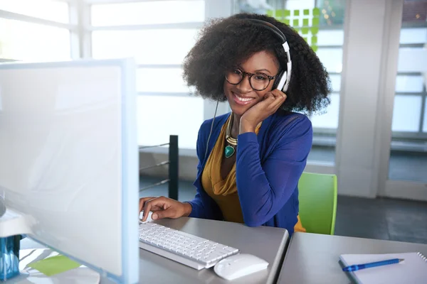 Retrato de uma mulher sorridente com um afro no computador em escritório de vidro brilhante — Fotografia de Stock