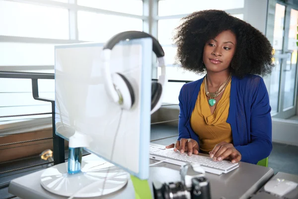 Ritratto di una donna sorridente con un afro al computer in un luminoso ufficio di vetro — Foto Stock