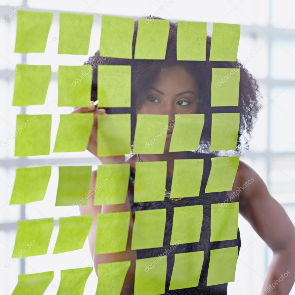 Portrait of a business woman with an afro behind sticky notes in bright glass office