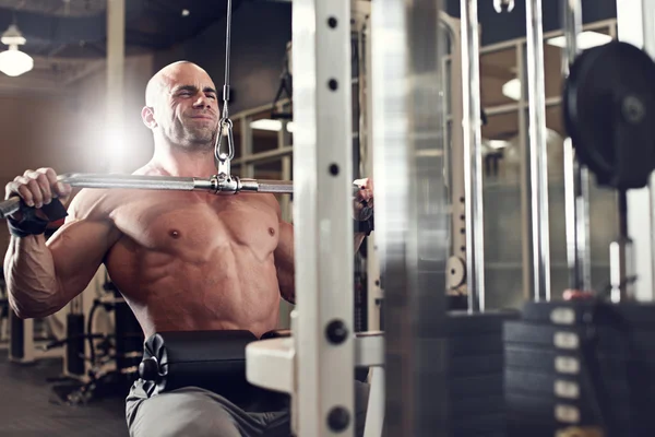 Fisicoculturista haciendo ejercicio en el gimnasio mientras usa la máquina de fitness —  Fotos de Stock