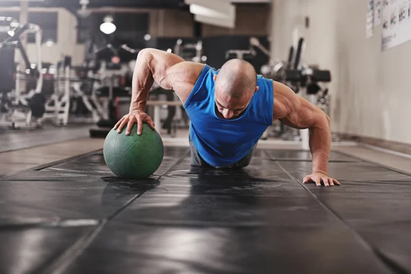 Bodybuilder working out and doing push upsat the gym while — Stock Photo, Image