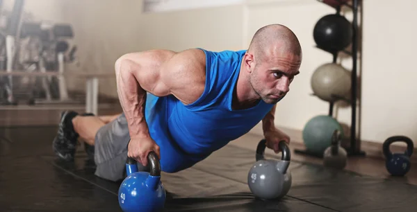 Bodybuilder working out and doing push upsat the gym while — Stock Photo, Image