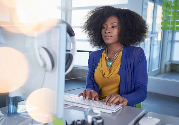 Portrait d'une femme souriante avec un afro à l'ordinateur dans un bureau en verre lumineux — Photo