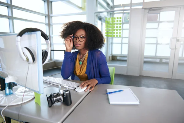 Retrato de uma mulher sorridente com um afro no computador em escritório de vidro brilhante — Fotografia de Stock