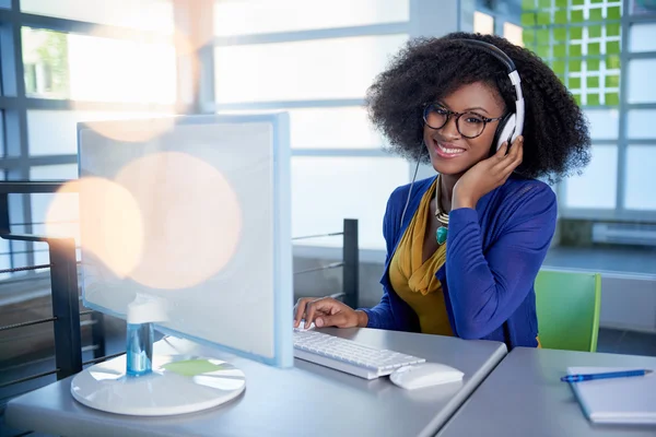 Ritratto di una donna sorridente con un afro al computer in un luminoso ufficio di vetro — Foto Stock