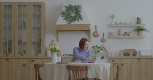 Joven mujer de negocios de 30 años que trabaja con documentos de papel y portátil en la cocina. Empresaria que trabaja desde casa. Mujer firmando documentos en casa oficina. — Vídeos de Stock