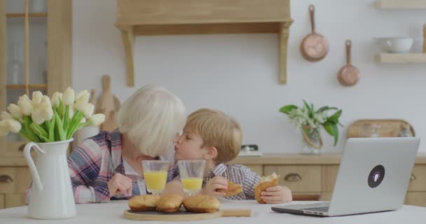 Ηλικιωμένη γυναίκα και παιδί να κολλάνε πέντε ενώ τρώνε ψωμάκια καθισμένοι στο τραπέζι της κουζίνας. Η οικογένεια διασκεδάζει απολαμβάνοντας σπιτικά γλυκά. — Αρχείο Βίντεο
