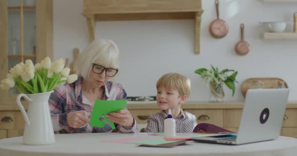Büyükannem evde anaokulu torunuyla başvuruda bulunuyor. Aile mutfakta yapıştırıcı, makas ve renkli kağıtlarla yaratıcı aktiviteler yapıyor. Birlikte sanat yapmak.. — Stok video