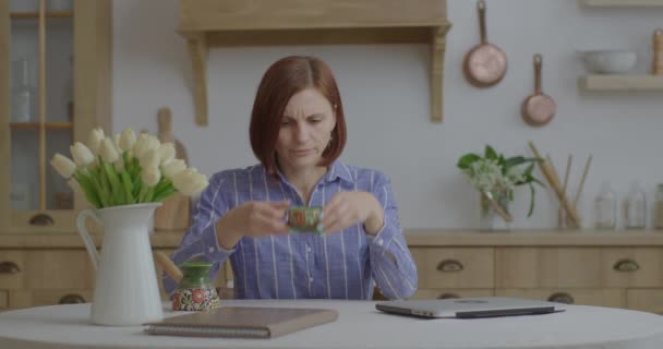 Jonge zakenvrouw uit de 30 typt op laptop en drinkt koffie in de keuken. Vrouwelijke ondernemer moe van online werken vanuit huis. Vrouw sluit laptop en geniet van koffie. — Stockvideo