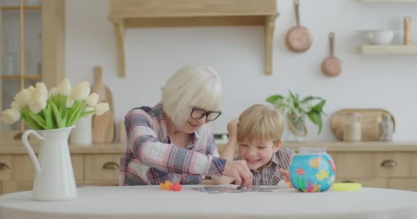 Blonde granny playing board game with preschool grandson at wooden kitchen. Happy senior woman and kid having fun staying at home. — Stock Video