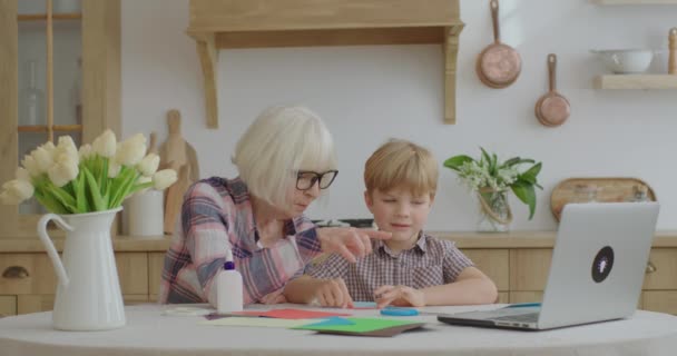 Büyükannem ve torunum internetten evde başvuru yapmayı öğreniyor. Aile mutfakta renkli kağıt, yapıştırıcı ve makas kullanarak yaratıcı aktiviteler yapıyor. Birlikte sanat yapmak.. — Stok video