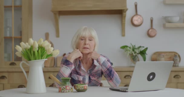 Senior 70er jaren vrouw toont verschillende emoties kijkend naar camera zittend aan keukentafel. Oudere vrouw toont verrassing, bewondering, verdriet, onenigheid en duim omhoog. — Stockvideo