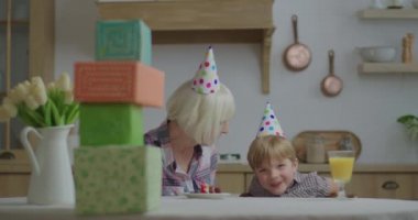 Anaokulu öğrencisi şapkalı çocuk evde elinde hediyelerle büyükannesiyle konuşuyor. Aile doğum gününü evde kutluyor..
