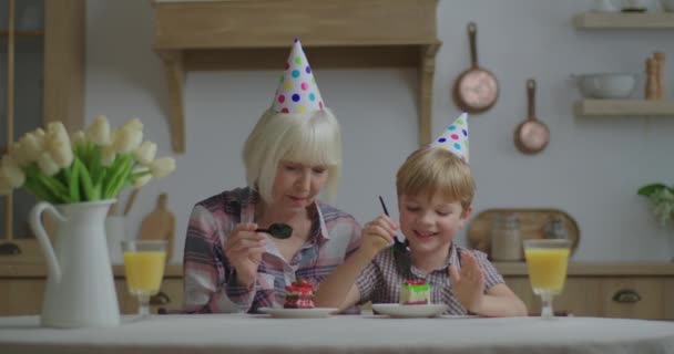 El niño preescolar en sombrero de fiesta celebra su cumpleaños en casa. Familia comiendo cada uno de los otros pedazo de pastel de cumpleaños. Casa fiesta de cumpleaños. — Vídeo de stock