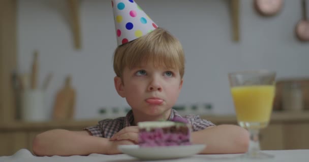 沉思的学龄前儿童看着一块蛋糕悲伤地叹了口气的画像。孩子因为没有客人而不高兴.生日男孩一个人在家。靠近点. — 图库视频影像