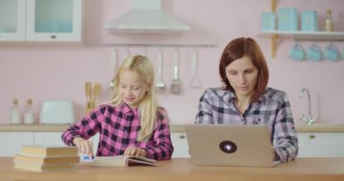 Ödev yapan liseli kız ve dizüstü bilgisayarda yazan anne. Aile evde birlikte kalır. Pembe mutfakta oturan çocuklu bir anne olarak çalışıyorum..