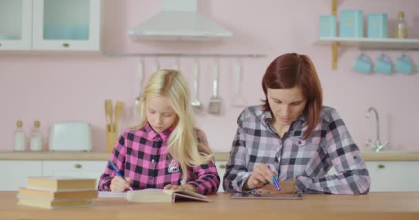 タブレットコンピュータと女子校生を使って働く母親が学校の宿題を近くで作っている。家族の仕事や家庭から勉強。ママと娘は家にいて. — ストック動画