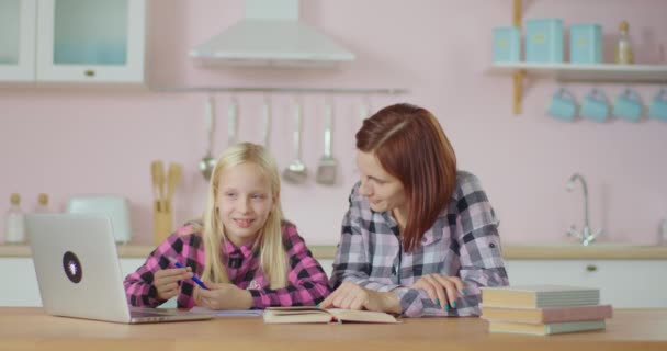 Familia feliz hablando de la escuela sentada en la cocina rosa. Chica contando historias de madre mientras estudia. Joven mujer adulta escuchando a niño. — Vídeo de stock