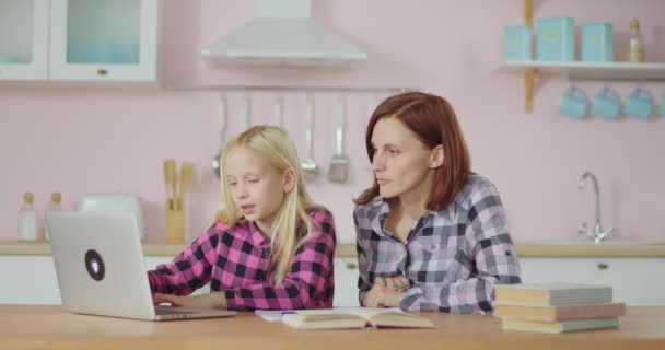 Dijital eğitim için dizüstü bilgisayar kullanan 30 'lu yaşlarda bir anne kızını izliyor. Çevrimiçi eğitim ve uzaktan öğrenme süreci. Evde eğitim. — Stok video