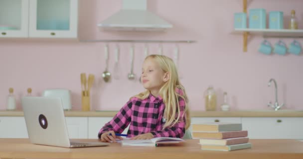 Schoolgirl memiliki pelajaran online di rumah. Anak-anak belajar online di laptop. Girl menulis dan menunjukkan notebook dengan jawaban untuk guru online. — Stok Video