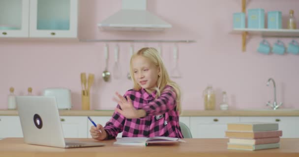 La colegiala tiene clase en línea en casa. Niño estudiando en línea en el ordenador portátil y anotando tareas para el profesor en línea. Niño con libros de texto de la escuela en casa. — Vídeo de stock