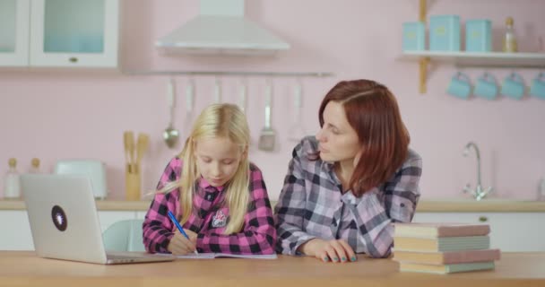 Rodina třicetileté matky a desetileté dcery si dělají domácí úkoly na dálkové studium. Dívka píše perem do sešitu, žena se dívá. Máma pomáhá klukovi se školními úkoly. — Stock video