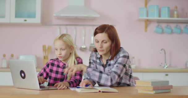 Chica preadolescente escribiendo en el ordenador portátil con la madre joven ayudando con el libro de texto. Familia haciendo deberes juntos en casa. — Vídeo de stock