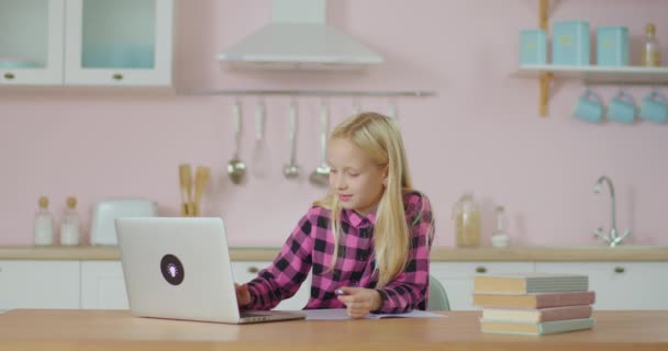 П'ятнадцять дівчат навчаються онлайн, перебуваючи вдома. Малюк друкує на ноутбуці і робить нотатки в блокноті. Шкільна дитина з гаджетом . — стокове відео