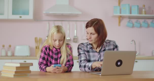 Joven mamá y su hija riendo mientras ve contenido divertido en la aplicación de teléfono móvil. Familia navegando por Internet y sonriendo. Mujer y chica usando gadgets en casa. — Vídeo de stock