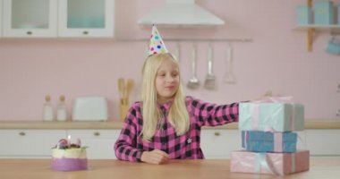 Doğum günü kızı hediyeleri açıyor ve evde kalıyor. Çocuk doğum gününü yalnız kutluyor. Doğum günü şapkası ve mumlu pastası olan tatlı sarışın kız.. 